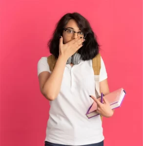 joven-colegiala-bastante-caucasica-sorprendida-auriculares-cuello-gafas-bolsa-trasera-pone-mano-boca-sosteniendo-libros-aislados