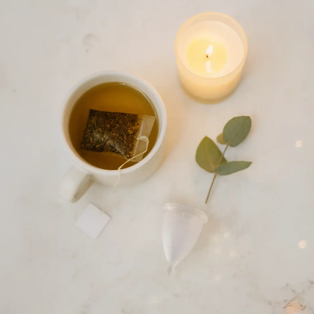 Un ritual nocturno para el descanso menstrual con una infusión caliente, una vela y una copa menstrual Angelcup limpia sobre una mesita de noche.