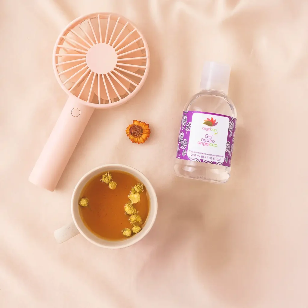 Elementos para aliviar los bochornos del climaterio: una taza de té herbal caliente junto a un pequeño ventilador de mano, simbolizando el autocuidado.