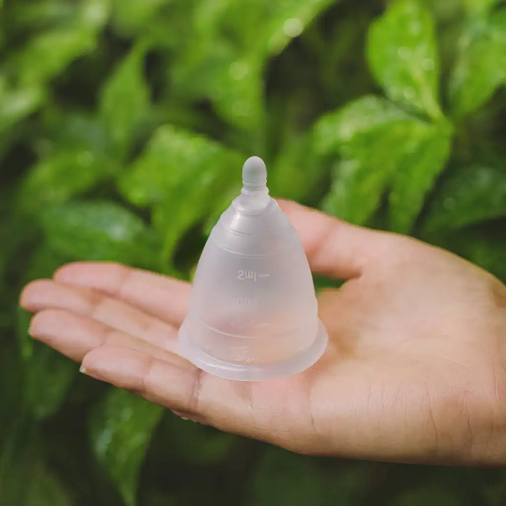 Mano sosteniendo una copa menstrual Angelcup transparente, simbolizando la conexión entre la menstruación consciente y el ahorro de agua.