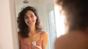 mujer sonriente sosteniendo copa menstrual frente a espejo reflejando la tranquilidad de haber aprendido como ponerse la copa menstrual