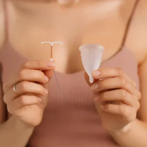 La copa menstrual y el DIU siendo sostenidos por una mujer en ambas manos mostrando las formas y tamaños de cada uno