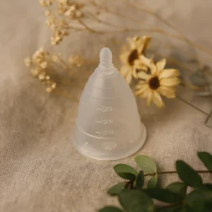 Copa menstrual Angelcup sobre una tela de lino junto a flores secas, simbolizando una menstruación sostenible y natural.