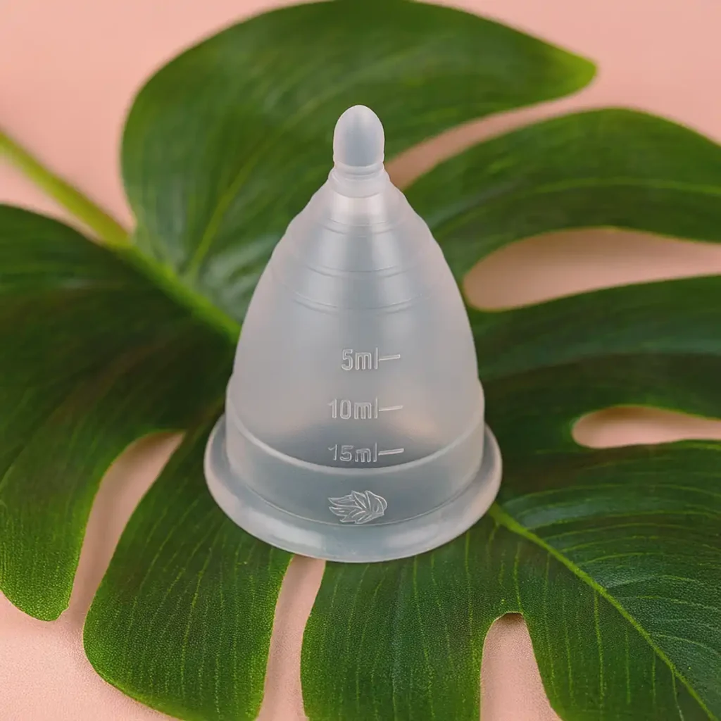 Copa menstrual Angelcup transparente mostrando su flexibilidad y pureza sobre una hoja verde, la principal alternativa ecológica para la menstruación sostenible.