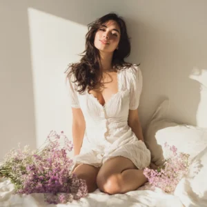 mujer con vestido blanco sentada en cama blanca con flores