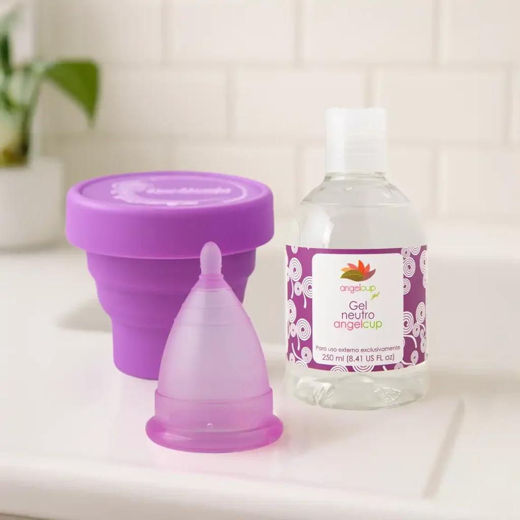 Kit de cuidado Angelcup con copa menstrual lila, vaso esterilizador morado y botella de gel neutro, en un ambiente de baño limpio y luminoso.