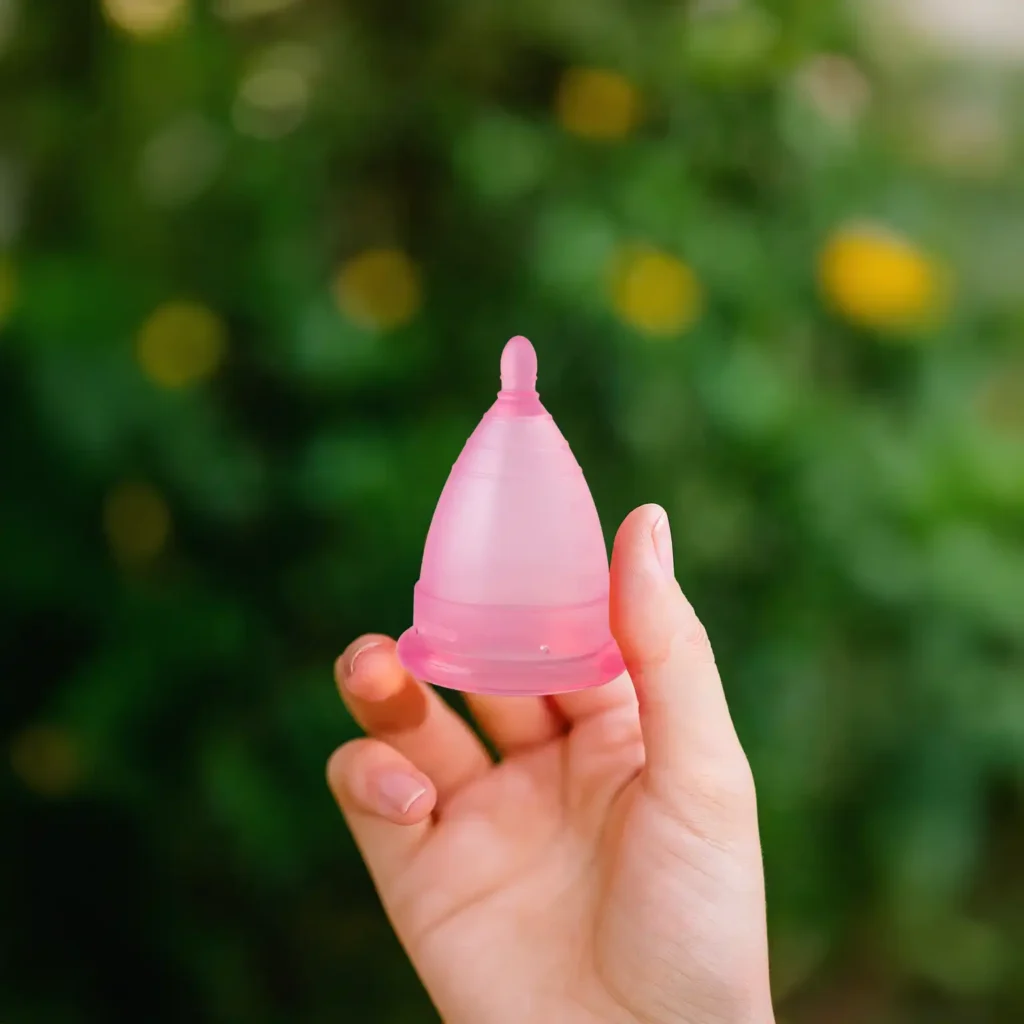 Mujer sonriendo en un campo verde sosteniendo una copa menstrual Angelcup, simbolizando el impacto ambiental de la copa menstrual positivo.