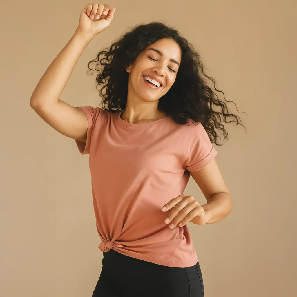 Mujer joven sonriendo y bailando con libertad, vestida con blusa rosa y pantalón oscuro sobre fondo neutro. La imagen transmite bienestar, confianza y alegría, símbolo de la libertad que ofrece Angelcup durante el ciclo menstrual.