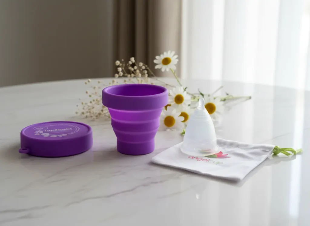 Set de Copa Menstrual Angelcup sobre mesa de mármol con esterilizador morado, bolsita de algodón y flores naturales, en una escena luminosa que transmite autocuidado, higiene íntima y bienestar femenino.