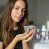 Mujer latina mostrando una copa menstrual Angelcup en sus manos, con productos de higiene íntima al fondo, en un ambiente luminoso que refleja autocuidado, bienestar menstrual y conexión consciente con el cuerpo.